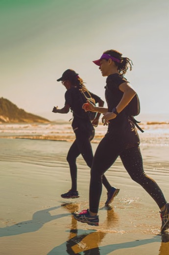 Two women running on a beach at sunrise